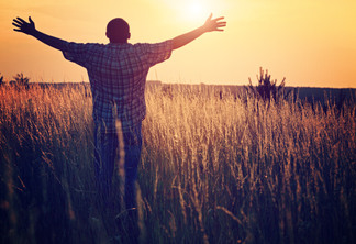 Man on the meadow prays to God. The man raises his arms to the sky, his face turned toward the sun. Freedom and religion symbol.