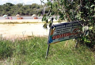 Placa de alerta sobre piranhas ficou “escondida” entre a vegetação perto da praia (Foto: Wenderson de Jesus)