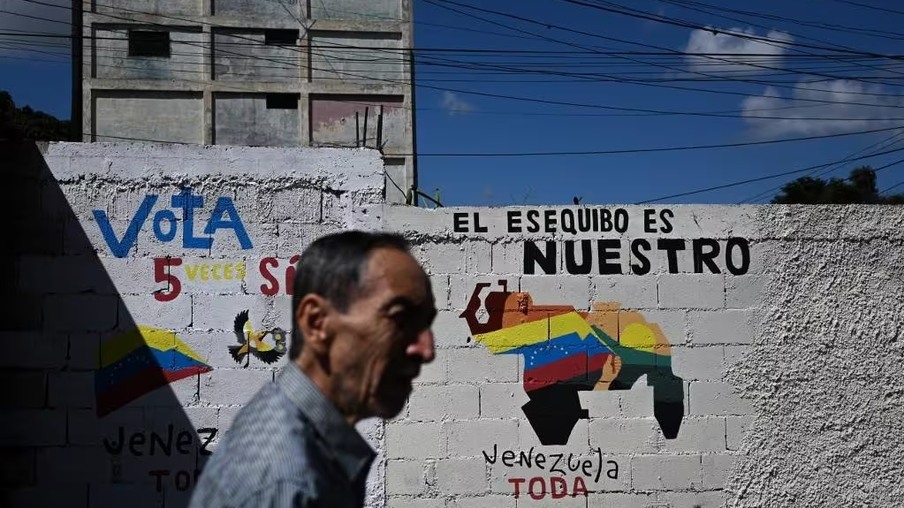 Venezuelano passa por muro onde está pintada uma campanha pela anexação de Essequibo — Foto: Federico PARRA / AFP